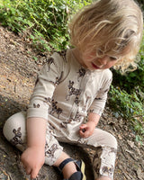 A toddler wearing a beige romper with a printed pattern of African Painted Dogs sitting on the ground.
