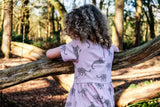 Girl wearing pink unisex organic cotton dress with leopard animal print in nature