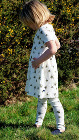 Girl wearing white organic cotton kid's dress and joggers with bee animal print