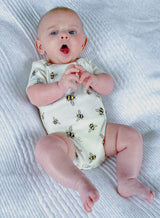 Yawning baby wearing white organic cotton bodysuit with bee animal print