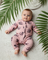 Baby lying on a textured surface with palm leaves, dressed in a soft pink sloth print organic cotton romper