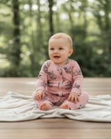 Baby sitting on a soft light blanket outdoors, dressed in pink organic cotton romper featuring a hand-drawn sloth print