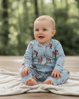 Smiling baby sitting on a cream blanket outdoors, dressed in a blue organic cotton romper featuring an all-over Exmoor pony print