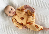 Baby lying on a pale textured blanket, dressed in orangutan print cotton romper with popper fastenings