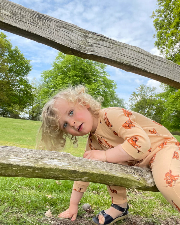 Baby wearing organic cotton orangutan romper outdoors, playing near a wooden fence in a green park