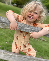 Baby in light peach orangutan print romper standing by a rustic wooden fence, showcasing front snap fastening